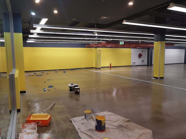 Commercial interior painting in progress by Colourise Painting for a large Sydney industrial space with yellow walls, polished concrete floors and ceiling lighting.